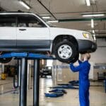 Mechanik ogląda białe auto terenowe na podnośniku w warsztacie