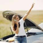 Kobieta przy zepsutym aucie z otwartą maską dzwoni po pomoc