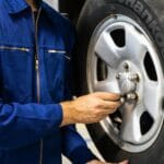 Mechanik w niebieskim kombinezonie sprawdza oponę w warsztacie samochodowym