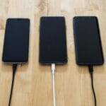 Trzy smartfony ładujące się na drewnianym blacie