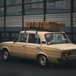 Beżowy sedan z bagażem na dachu jedzie autostradą w kierunku miasta