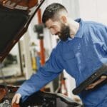 Mechanik w niebieskim kombinezonie sprawdza silnik używanego auta w garażu