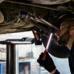 Mechanik z latarką sprawdza podwozie auta w warsztacie