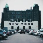 Parking z zaparkowanymi autami przy budynku z napisem New York