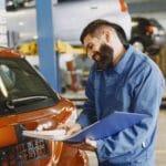 Uśmiechnięty mechanik w warsztacie sprawdza auto i trzyma dokumenty