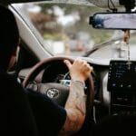 Wytatuowane ramię kierowcy na kierownicy Toyoty w słoneczny dzień