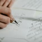 Dłoń kaligrafuje elegancki napis na papierze do zaproszeń ślubnych