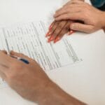 Dłonie podpisujące formularz na białym biurku