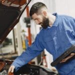 Mechanik w niebieskim kombinezonie sprawdza silnik auta w warsztacie