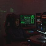 Mężczyzna w czarnej bluzie pracuje nad cyberbezpieczeństwem przy monitorach