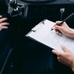 Osoba w samochodzie wypełnia formularz na podkładce obok dźwigni zmiany biegów