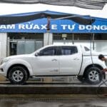 Mężczyzna myje białego pickupa myjką ciśnieniową w automatycznej myjni