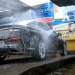 Mężczyzna myje czarne auto myjką ciśnieniową na zewnątrz